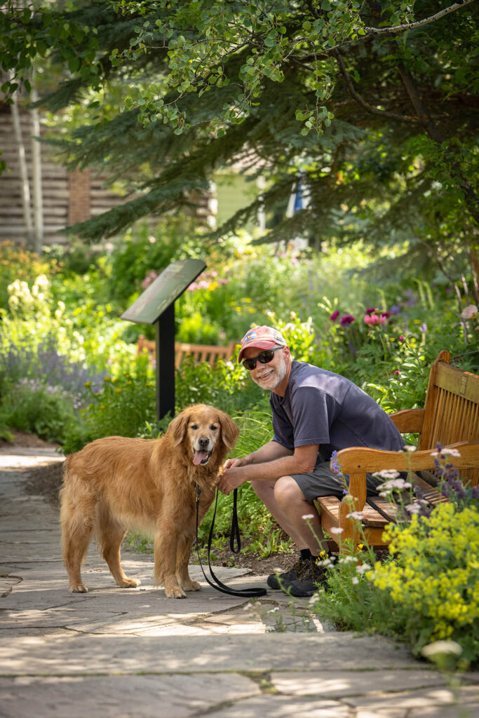 Man sitting on bench with his golden retriever at Betty Ford Garden in Vail