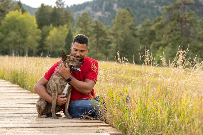 Dog and Owner Photoshoot. Man cuddling Boxer dog in mountains