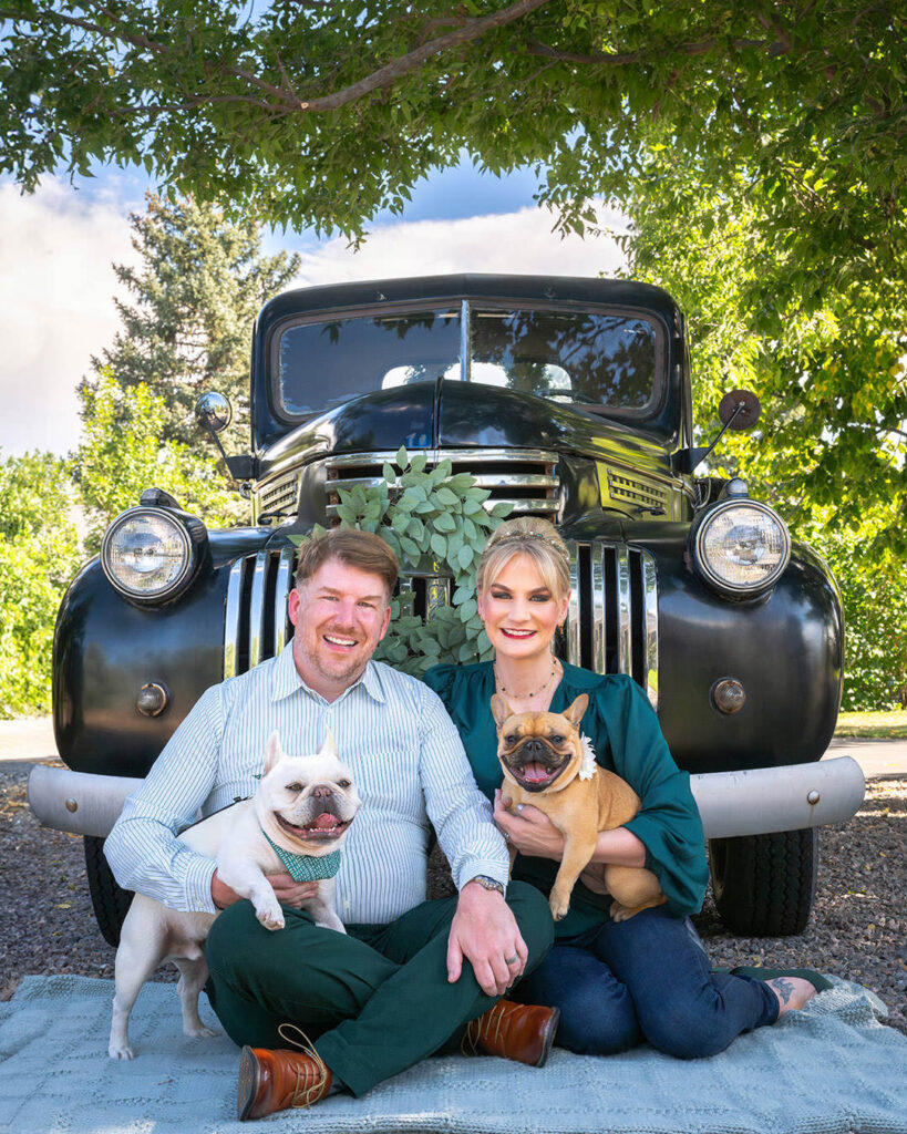 Two Frenchie dogs and couple in front of a black 1946 Chevy pickup truck