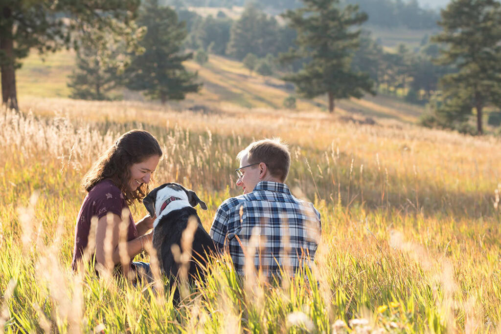 Couple posing for candid photo with their dog in between them in fall scene at White Ranch Park in Golden, Colorado