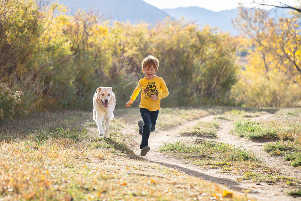 Six-year-old boy with yellow shirt and red hair running on dirt path near mountains with his yellow dog