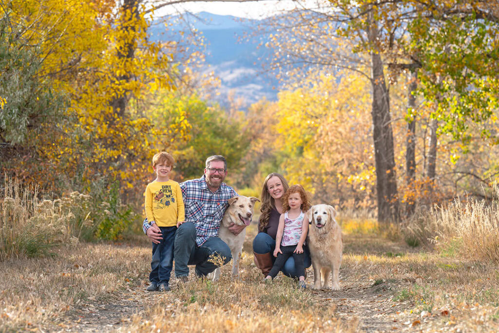 Family portrait with two dogs, mom, dad, son and daughter. There's Colorado mountain scenery with fall colors on the trees