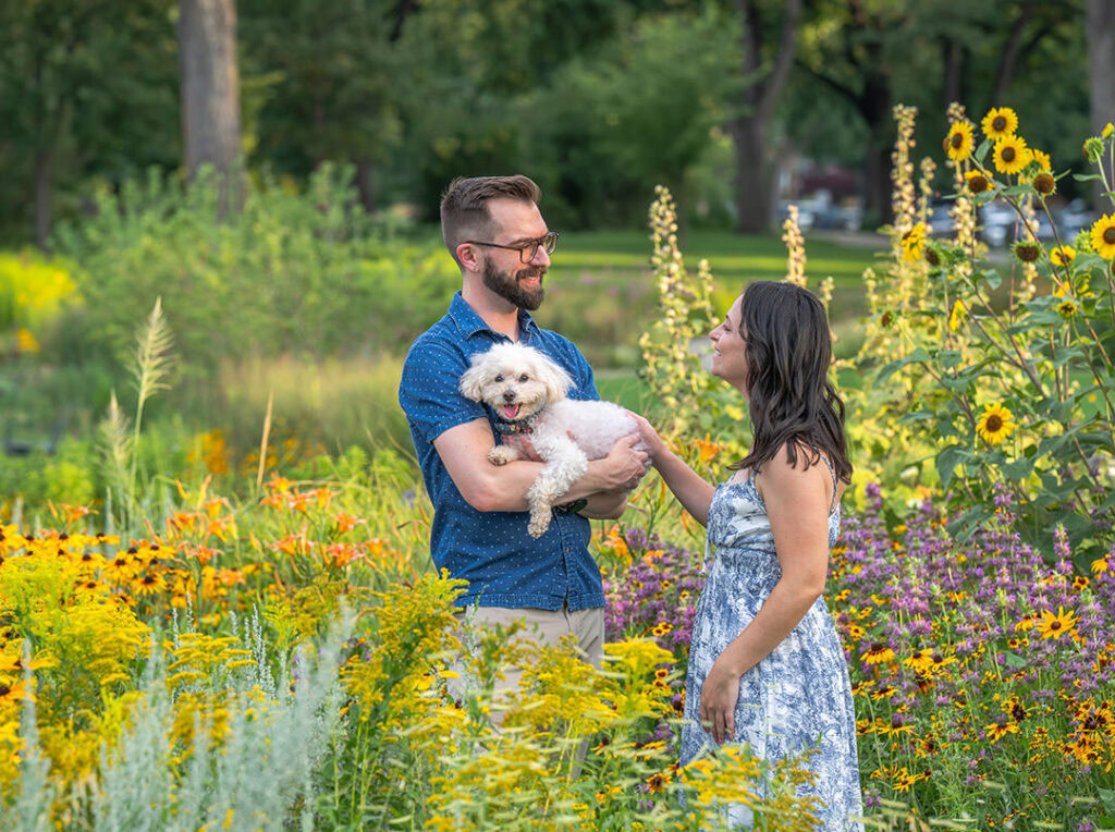 Young couple with their white miniature poodle dog in the Big Garden at Washington Park in Denver with lots of yellow flowers