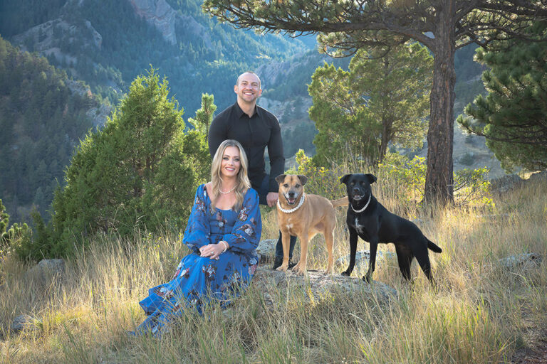 Outdoor family portrait with couple in formal dress and dogs in nature mountains and trees with dramatic sunbeams