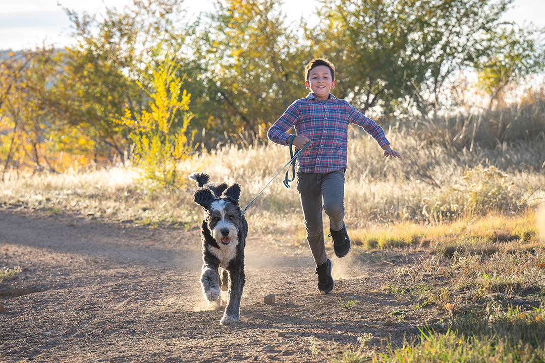 Boy running with Bernedoodle dog on leash during photoshoot in foothills