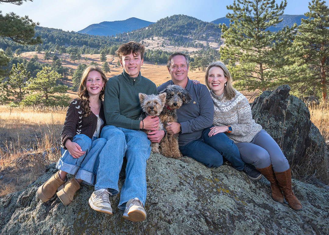 Family portrait sitting on rock with teens and parents and two small dogs