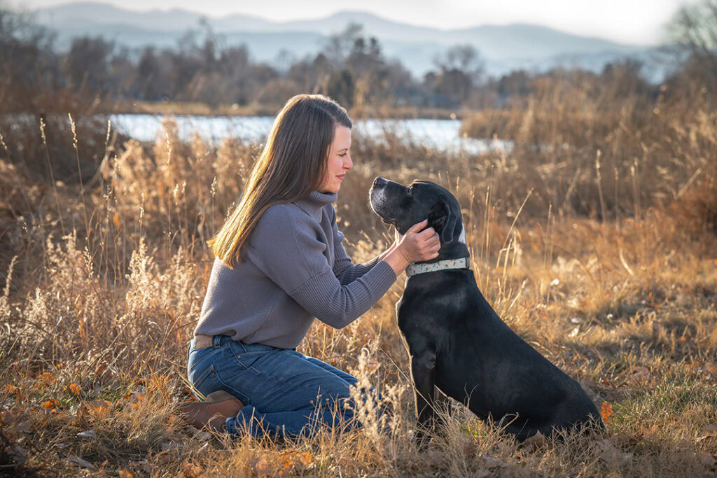 Profile of a woman looking into face of an older black dog in late fall with lake and mountains in background